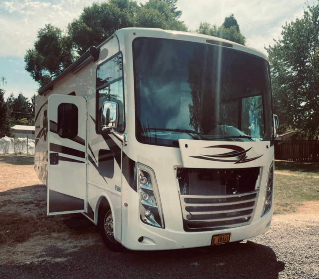 A gas Class A motorhome with its front access hatch open for an onsite oil change